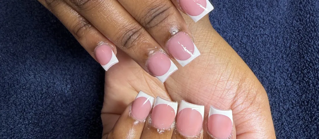 Classic pink-and-white French manicure on a navy towel.